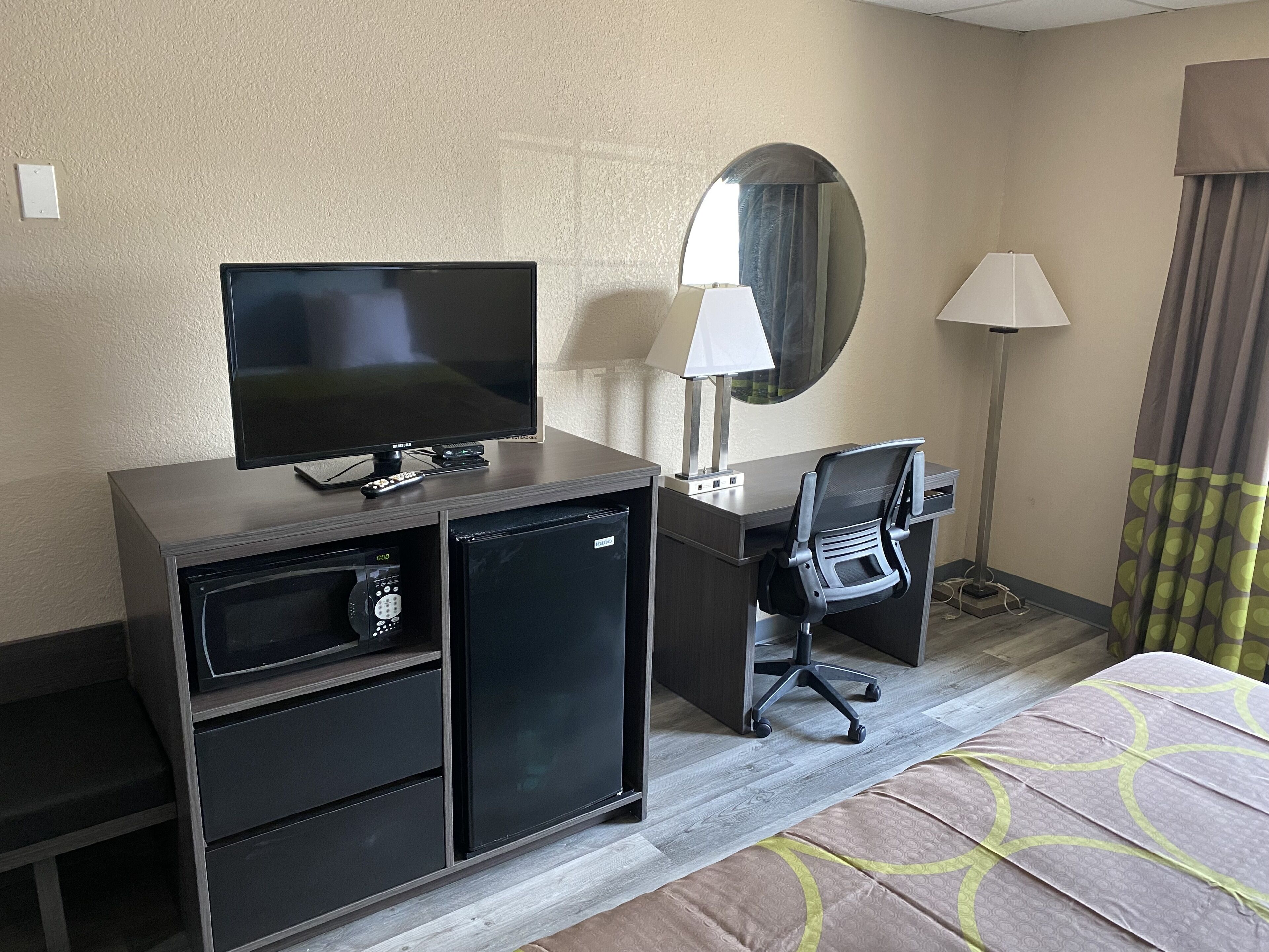 A hotel room with a TV, desk, chair, lamp, and a small refrigerator.