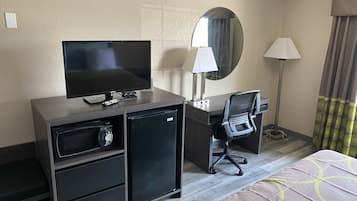 A hotel room with a TV, desk, chair, lamp, and a small refrigerator.