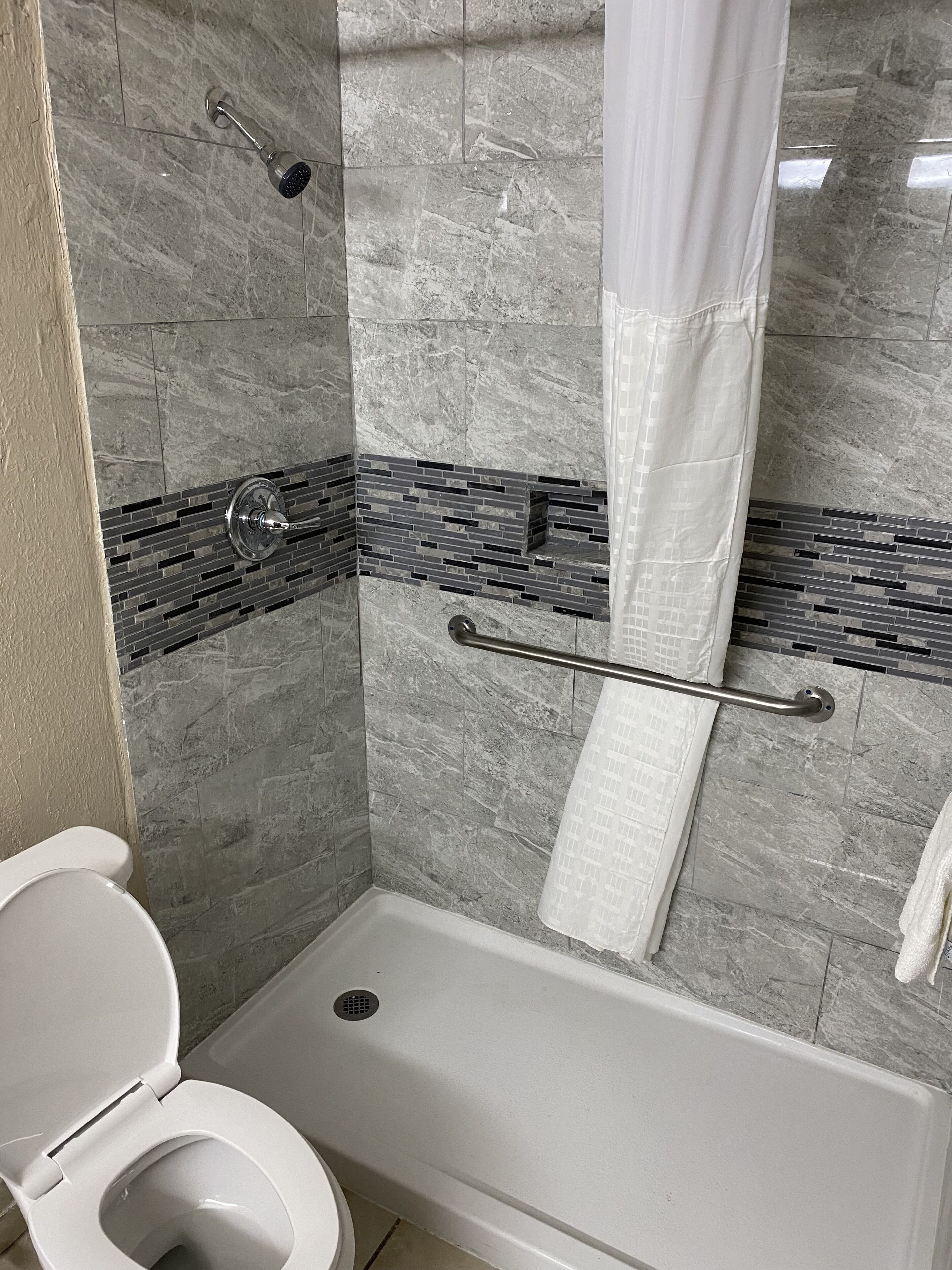 Un baño con ducha, inodoro y pared de azulejos con diseño de ladrillo.
