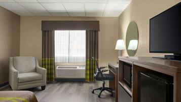 Habitación de hotel con cama, escritorio con computadora, televisor, aire acondicionado y ventana con cortinas.