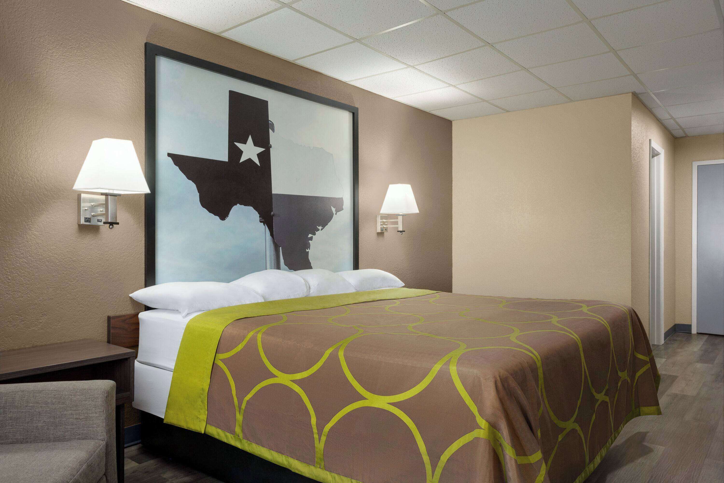 A hotel room with a large bed, two bedside lamps, a nightstand, and a wall-mounted map of Texas.