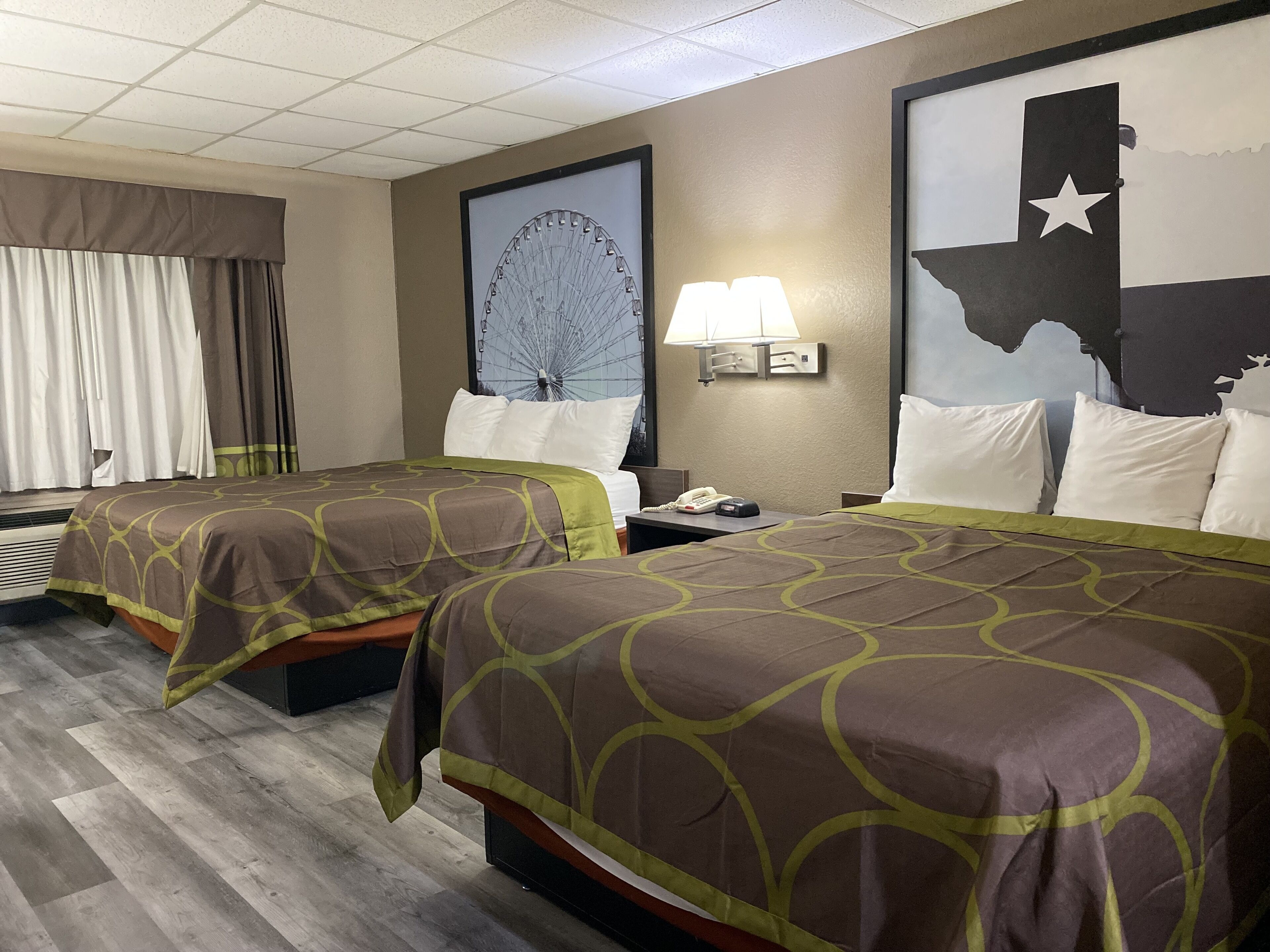 A hotel room with two beds, a large wall mural of a Ferris wheel, a lamp, and a nightstand with a phone.