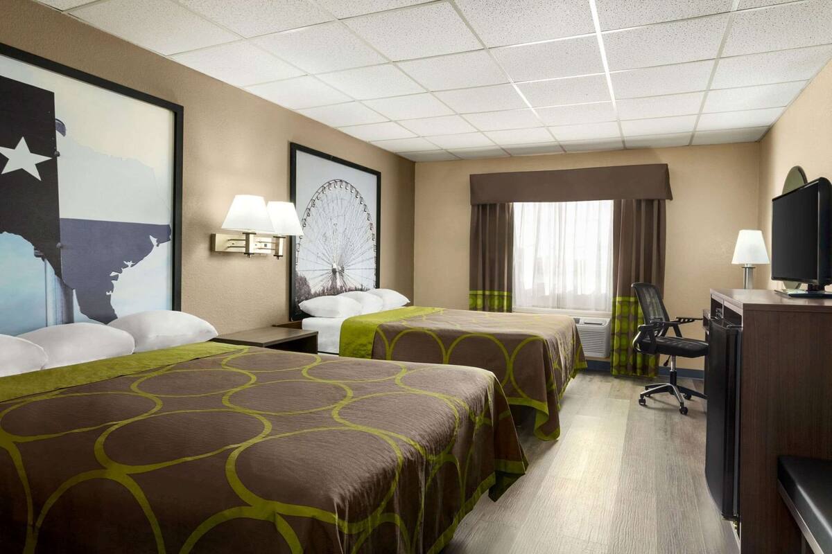 Ein Hotelzimmer mit zwei Betten, einem Schreibtisch, einem Fernseher, einem Fenster mit Vorhängen und einer Wand mit einer großen Karte und einem Bild von einem Riesenrad.