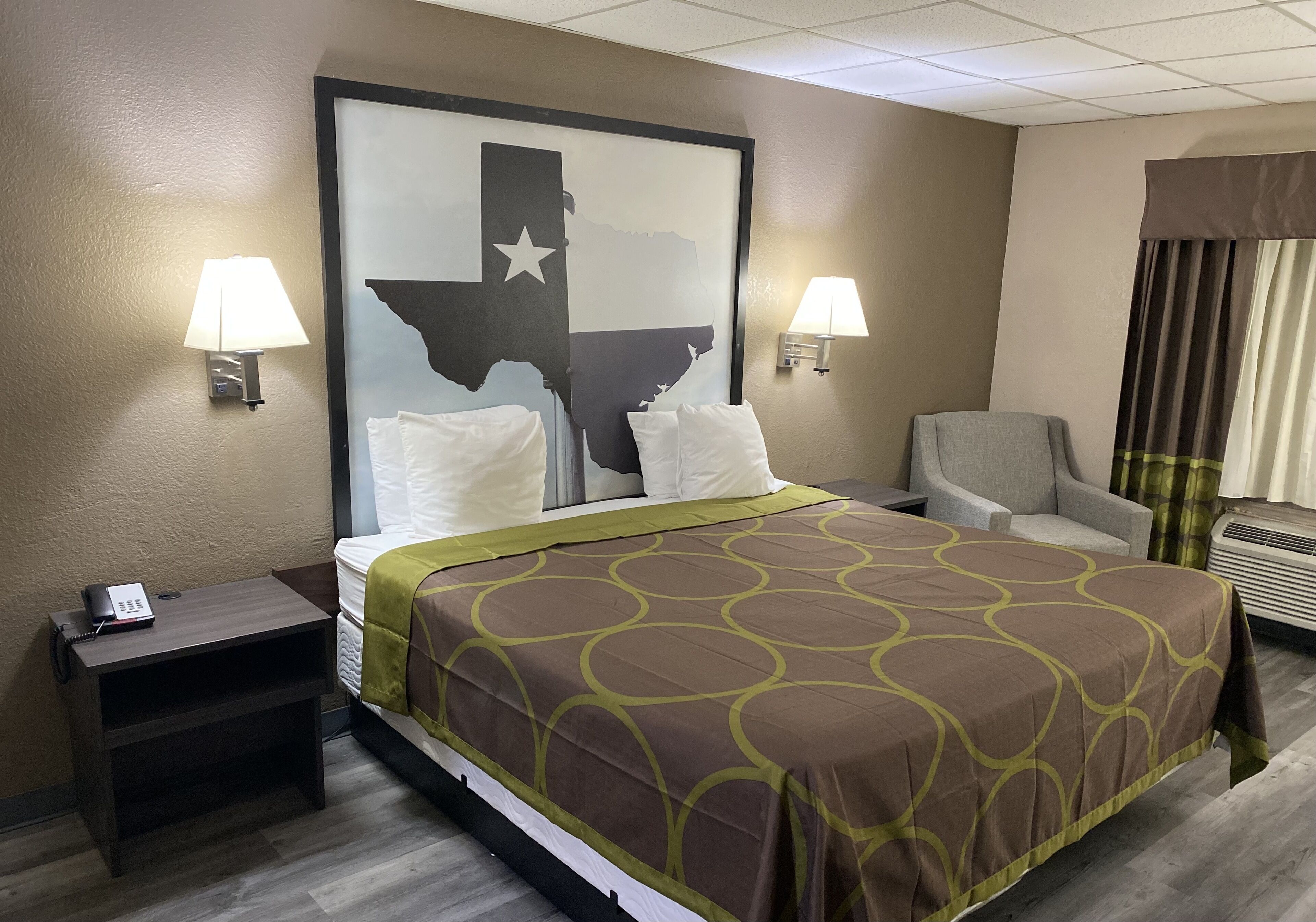 Una habitación de hotel con una cama grande, dos lámparas de noche, una silla, un escritorio con teléfono y un aire acondicionado instalado en la pared.