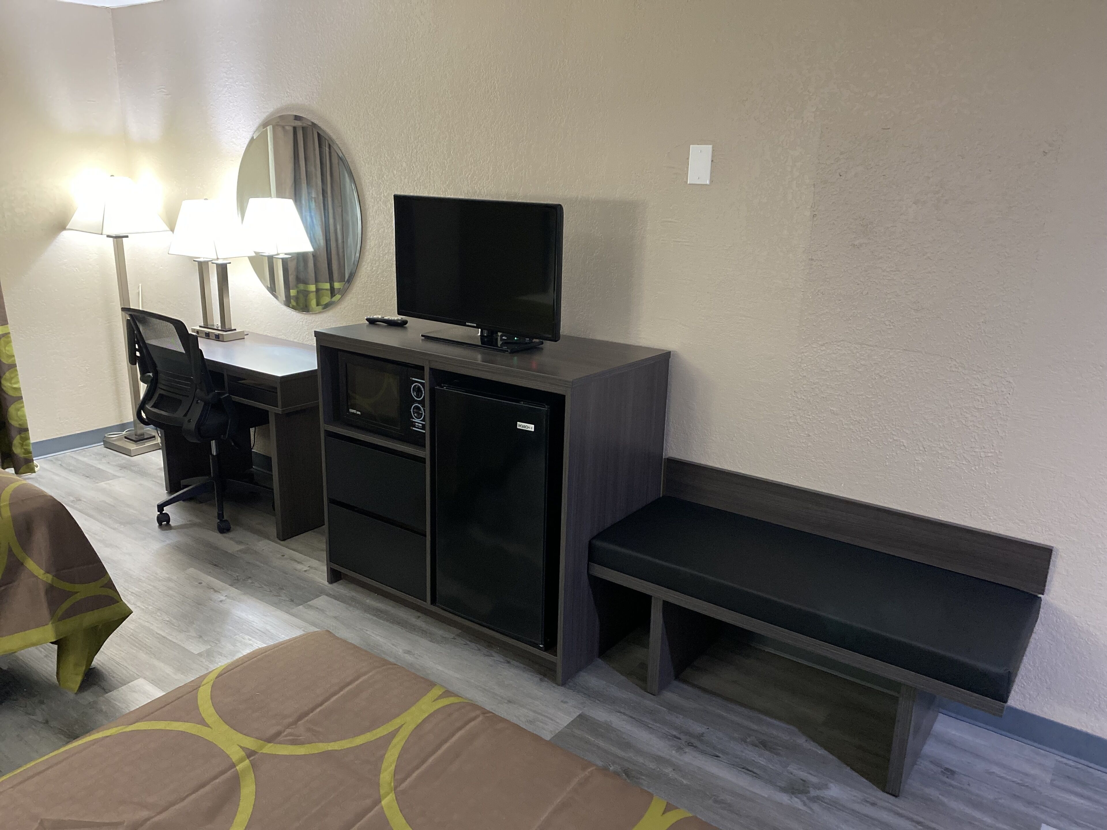 Une chambre d’hôtel équipée d’un bureau, d’une télévision, d’un four à micro-ondes, d’un réfrigérateur, d’une banquette et d’un lit recouvert d’une couvre-lit à motifs.