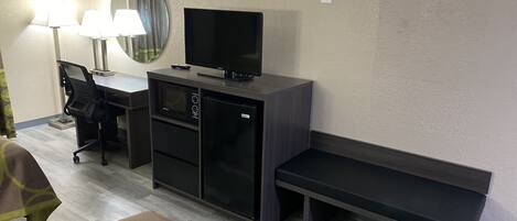 Une chambre d’hôtel équipée d’un bureau, d’une télévision, d’un four à micro-ondes, d’un réfrigérateur, d’une banquette et d’un lit recouvert d’une couvre-lit à motifs.