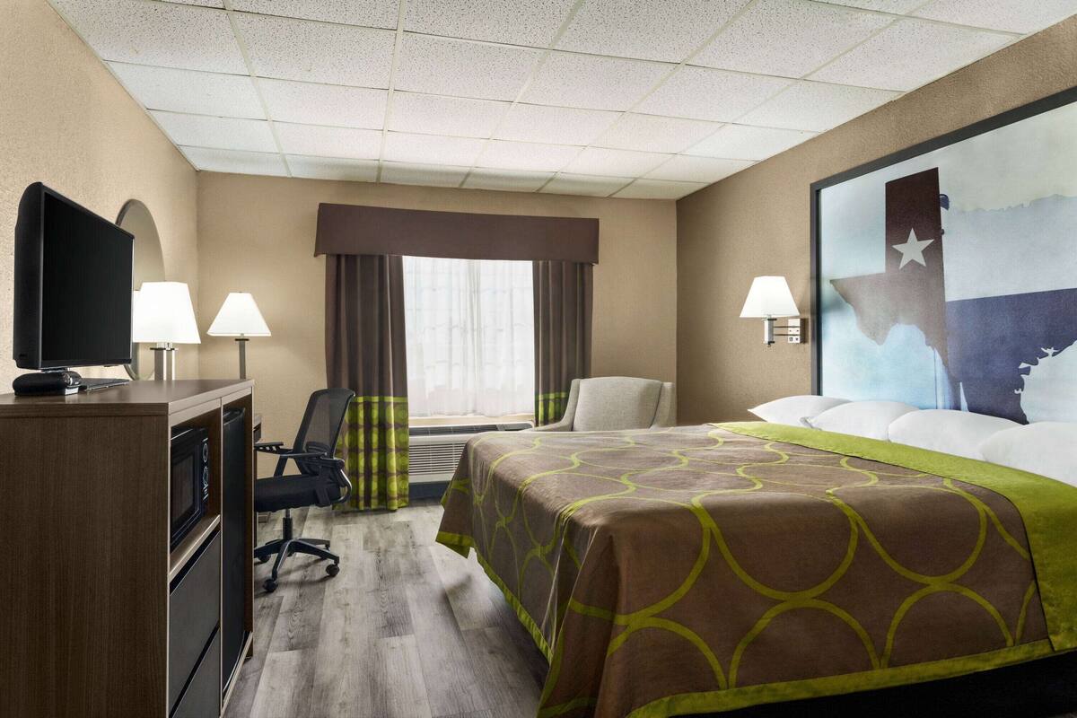 Ein Hotelzimmer mit Bett, Schreibtisch, Stuhl, Fernseher, Lampen und einem großen Fenster mit Vorhängen.