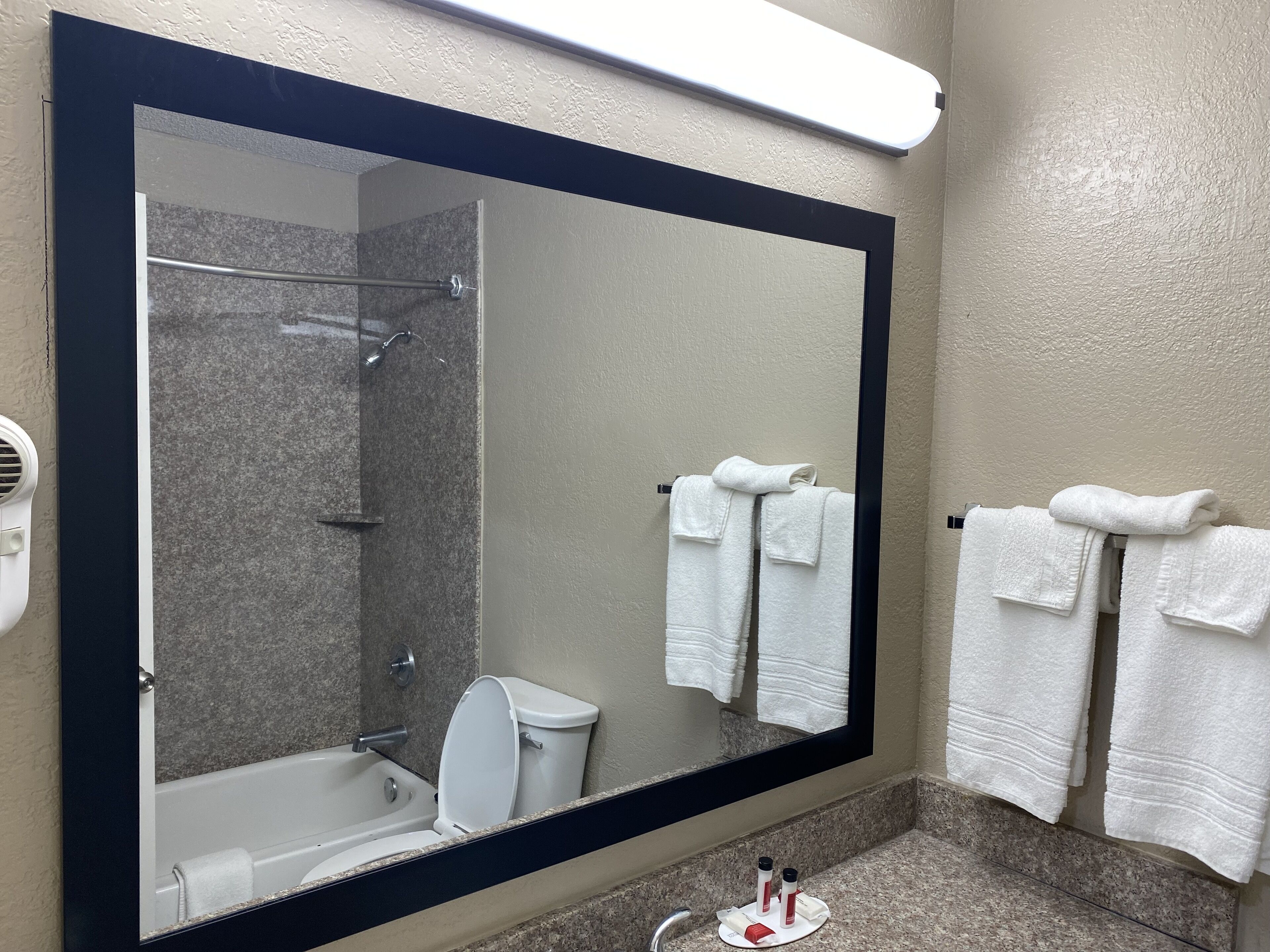 A bathroom with a large mirror, a bathtub, a shower, and two towels hanging on the wall.