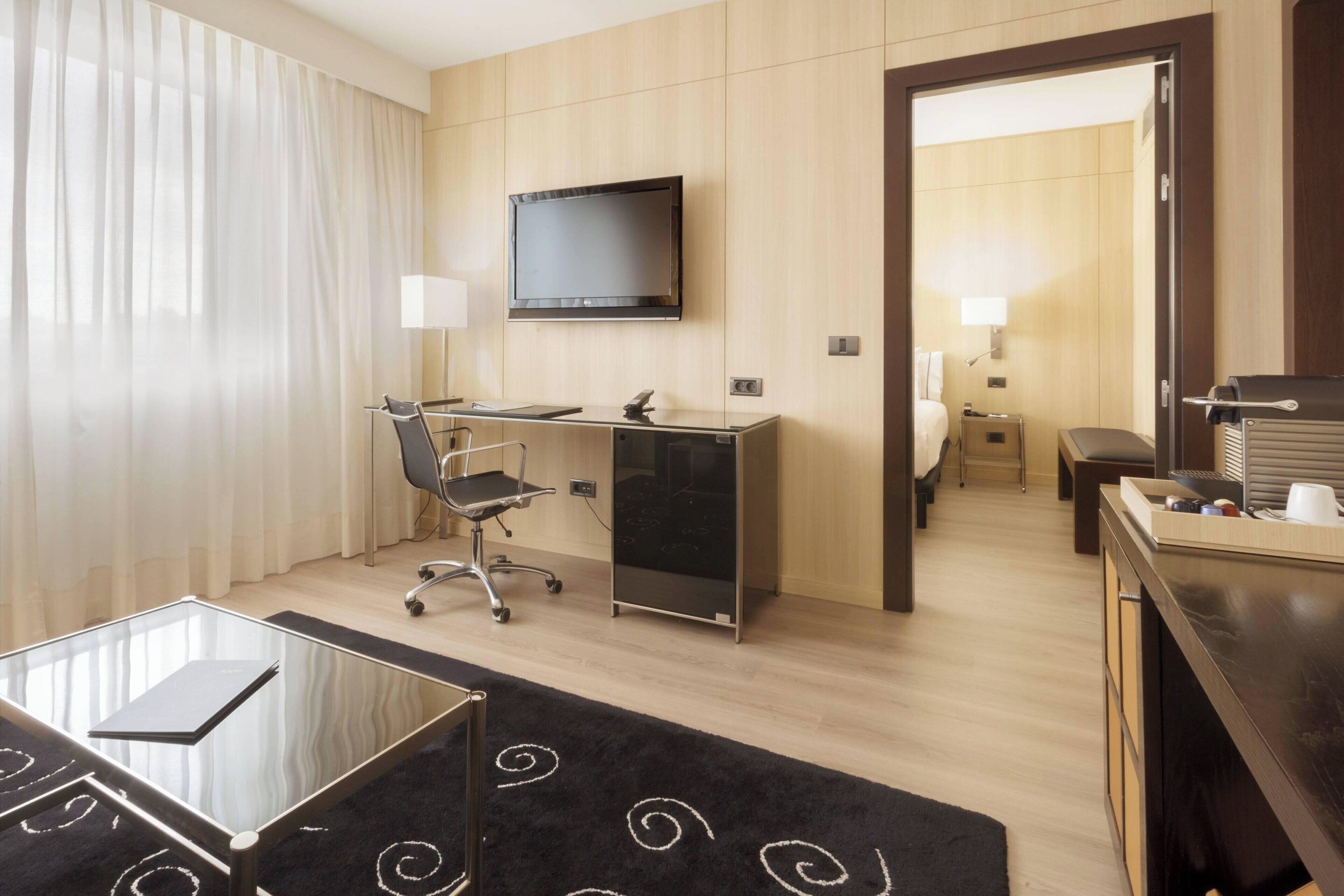 A hotel room with a desk, chair, TV, and a bed.