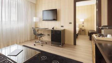 A hotel room with a desk, chair, TV, and a bed.