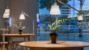 A modern indoor setting with round wooden tables and chairs, a potted plant on one table, and pendant lighting. - AC Hotel Córdoba by Marriott (Córdoba)