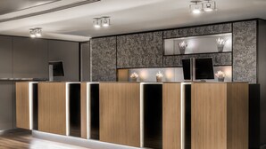A modern reception desk with a wooden finish, built-in TV, and potted plants. - AC Hotel Córdoba by Marriott (Córdoba)