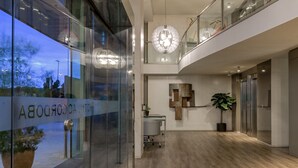 A modern hotel lobby with a glass wall, a reception desk, a potted plant, and a chandelier. - AC Hotel Córdoba by Marriott (Córdoba)