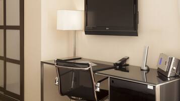 A hotel room with a desk, chair, television, lamp, and a small safe.