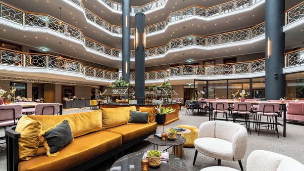 Een meerlaags atrium met een centraal zitgedeelte, compleet met een bank en fauteuils, omringd door tafels en stoelen.
