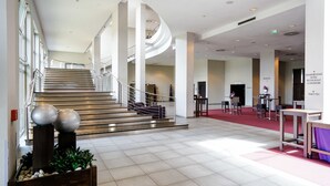 Een ruime hotellobby met een gebogen trap, een receptiebalie en een vloer bekleed met een rood tapijt.