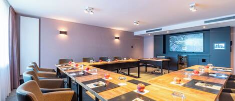 Un salón de conferencias con una larga mesa, varias sillas, una pantalla de proyector y una pantalla de presentación.