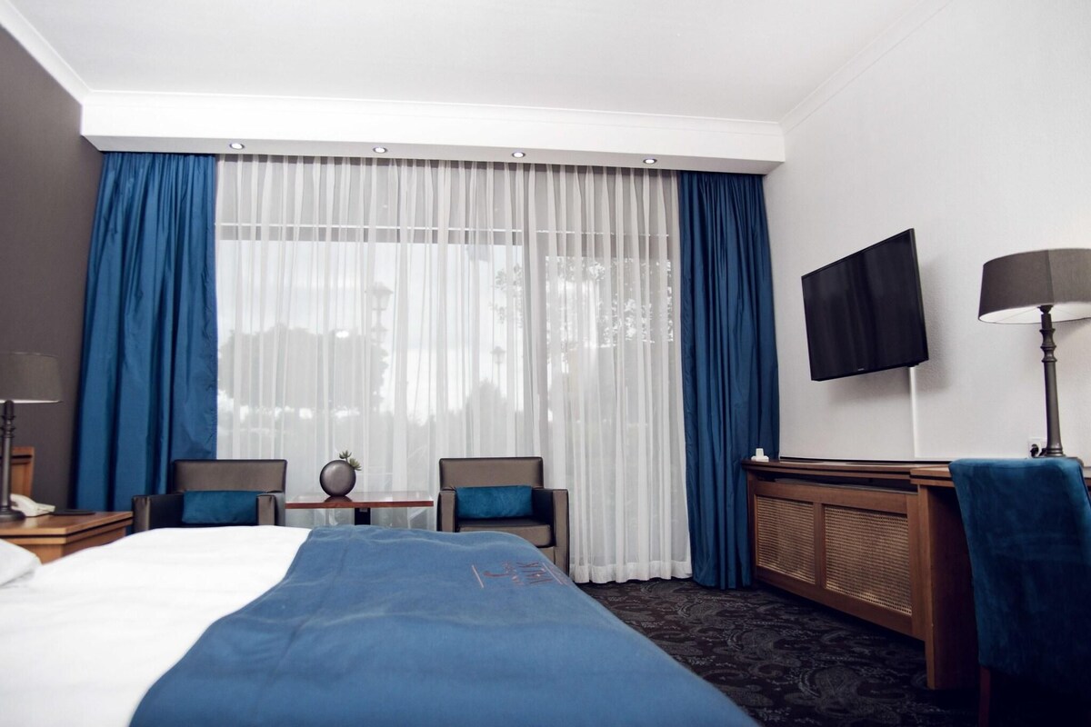 Une chambre d’hôtel avec un lit, deux chaises, une petite table, un téléviseur et une lampe.