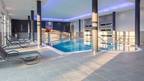 Een modern binnenzwembad met helder water, omgeven door zongedekte betegelde vloeren en ligstoelen.