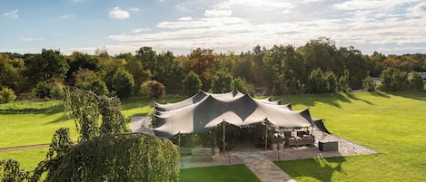 A tented outdoor area with a pathway leading to it, surrounded by greenery and trees.