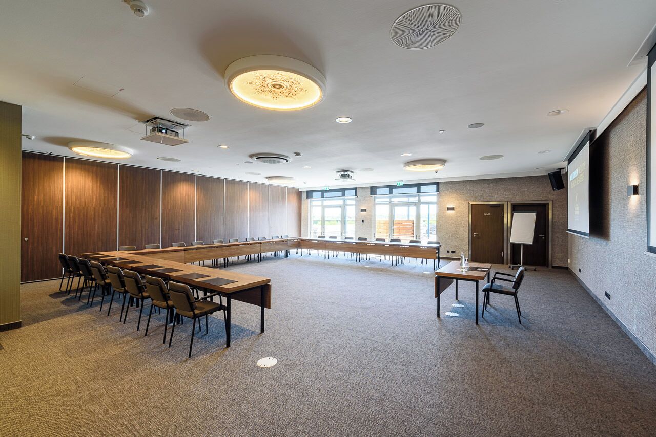 A conference room with a long table and chairs, large windows, and a projector screen.