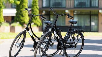 Duas bicicletas estacionadas em superfície pavimentada, com um edifício ao fundo.