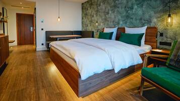 Una habitación de hotel moderna con una cama grande, una mesita de noche de madera, una silla verde y una pared con un diseño de hojas.