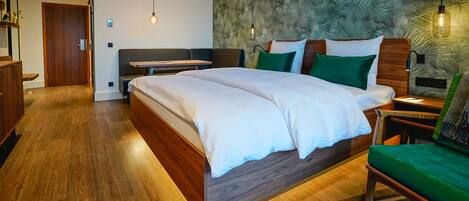Una habitación de hotel moderna con una cama grande, una mesita de noche de madera, una silla verde y una pared con un diseño de hojas.
