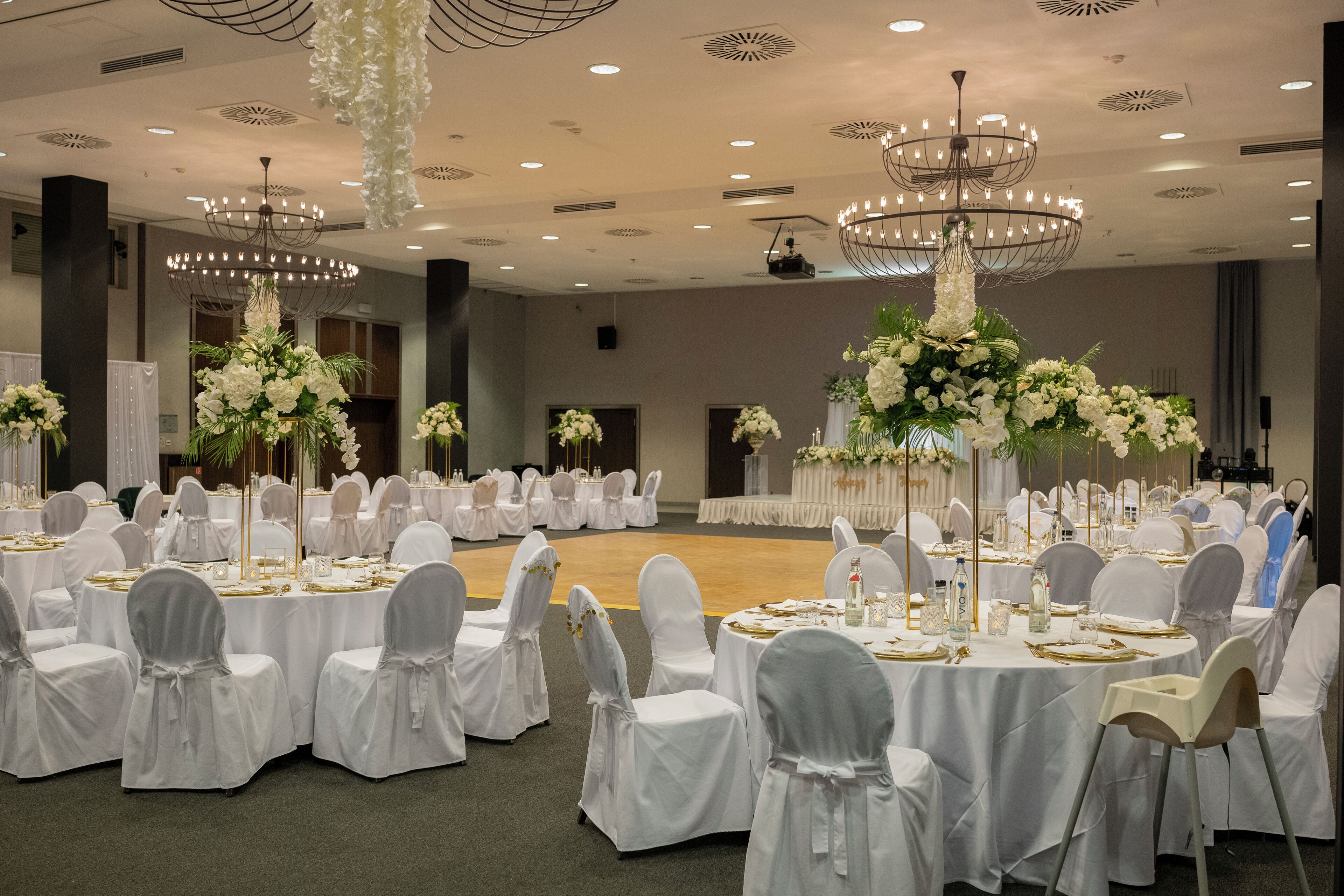 Un salón de banquetes con mesas redondas, manteles blancos y sillas con fundas blancas.