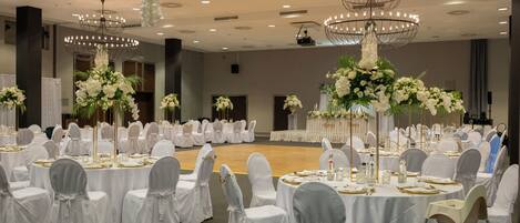 A banquet hall with round tables, white tablecloths, and chairs with white covers.