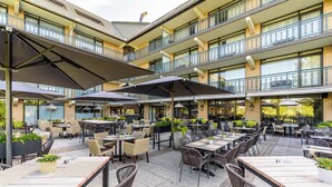 Een terras met meerdere tafels en stoelen, parasols en potplanten.