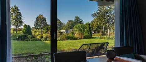A modern room with a large window, a sofa, a table, and a view of a well-maintained garden.