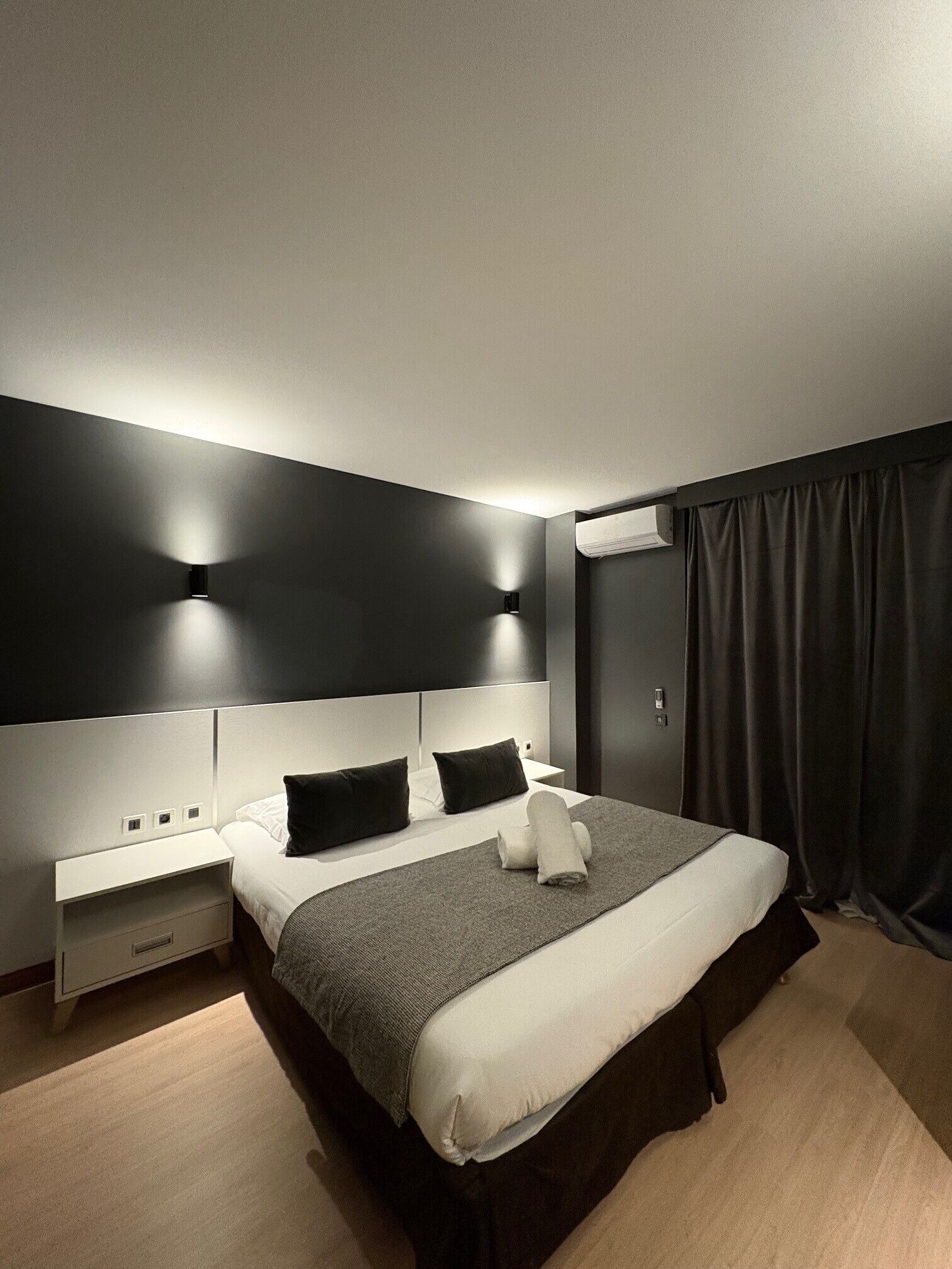 A modern hotel room with a large bed, bedside tables, and a dark curtain.