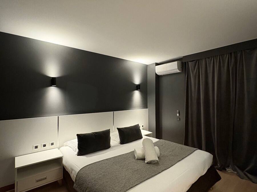 A modern hotel room with a large bed, bedside tables, and a dark curtain.