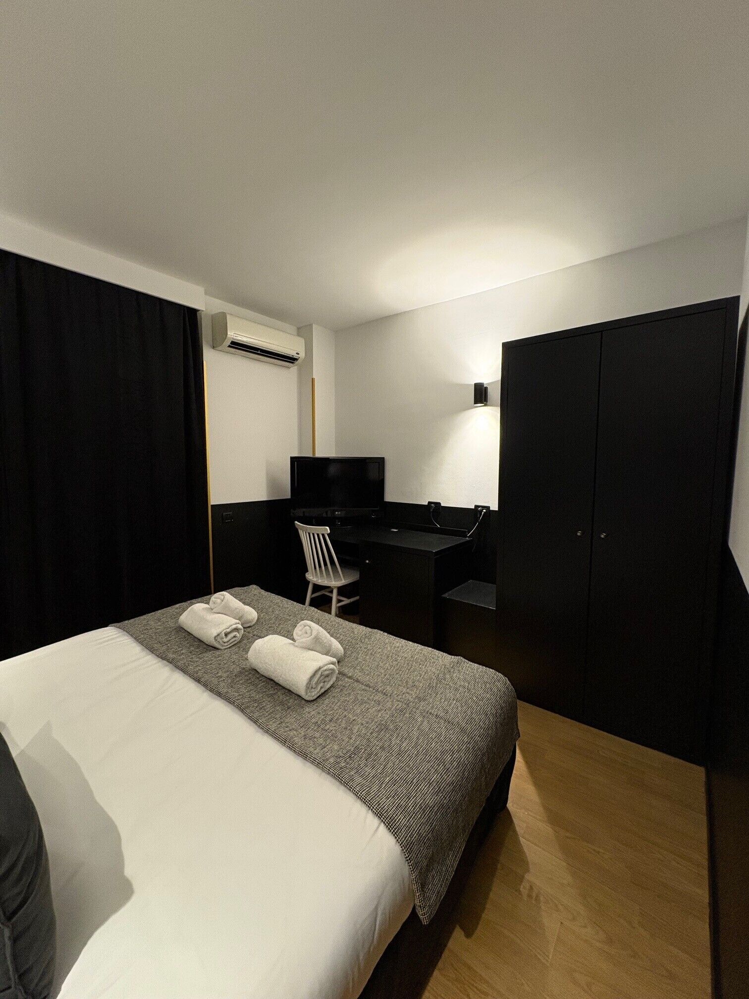 A hotel room with a bed, a desk, a chair, a TV, and a wardrobe.
