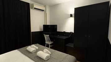 A hotel room with a bed, a desk, a chair, a TV, and a wardrobe.
