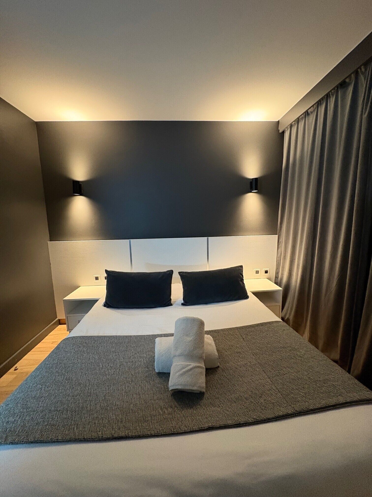 A modern hotel room with a large bed, two bedside tables, and a headboard with integrated lighting.