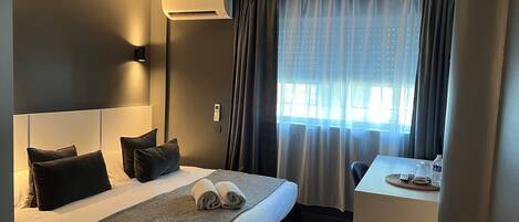 Et hotelværelse med en stor seng, et natbord, et skrivebord og et vindue med gardiner.