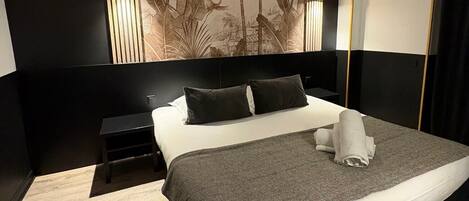 A modern hotel room with a large bed, a bedside table, a wall-mounted air conditioner, and a decorative wall panel.
