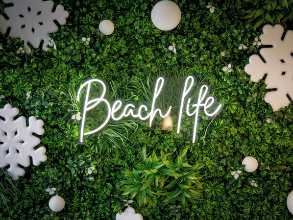 A neon sign that reads "Beach life" set against a backdrop of green foliage and decorative snowflakes. - Hôtel Locarno Nice (Nice)