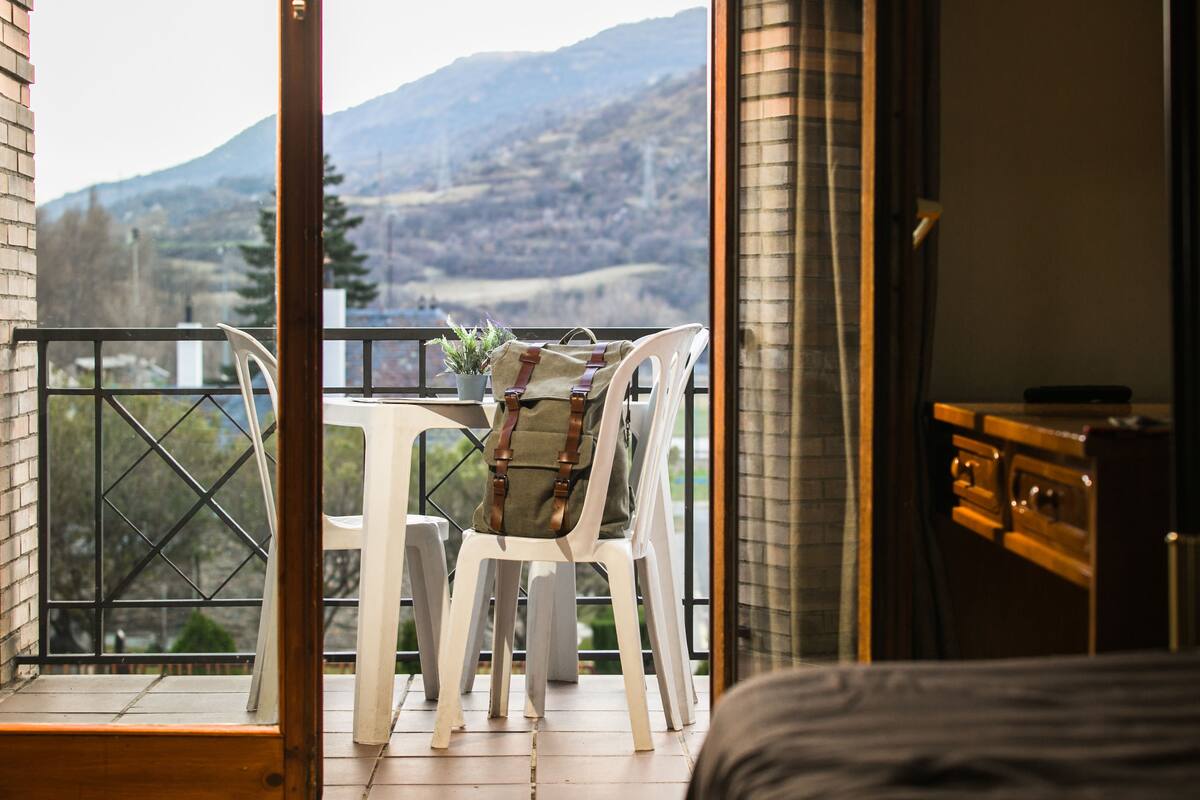 A balcony with a table and chairs, a potted plant, and a view of mountains.