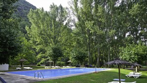 Une piscine entourée de pelouse et d’arbres, avec des chaises longues et des parasols.