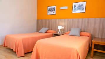 Una habitación con dos camas, cada una con colcha y almohadas anaranjadas a juego, una mesita de noche de madera con lámpara, y dos cuadros en la pared naranja.