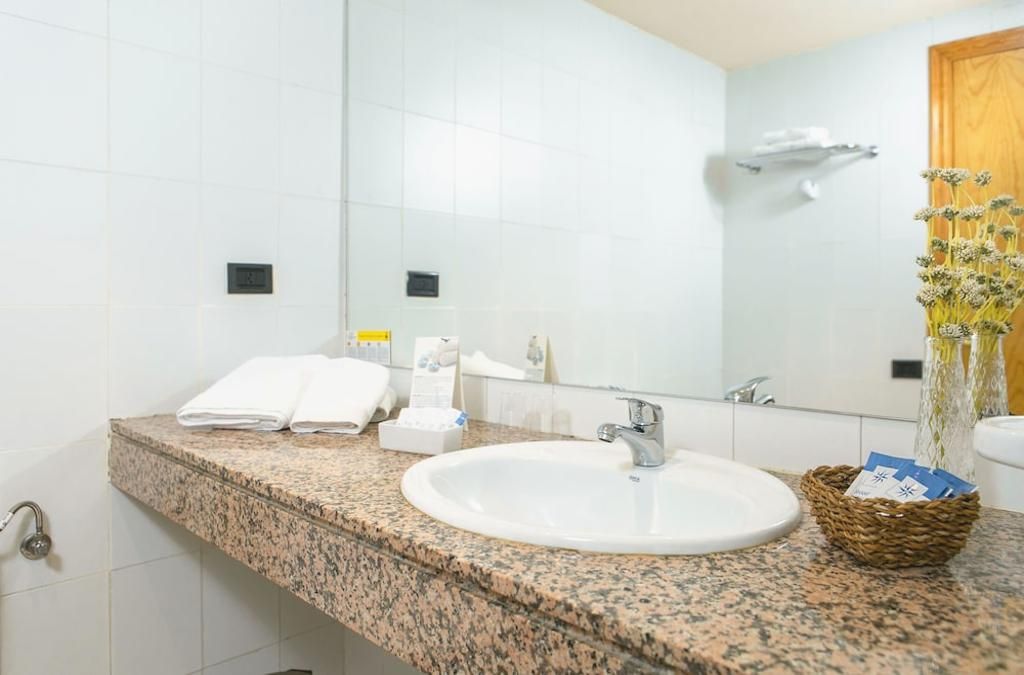 Un baño con encimera de granito, lavabo blanco y espejo. Hay toallas y artículos de aseo en la encimera.