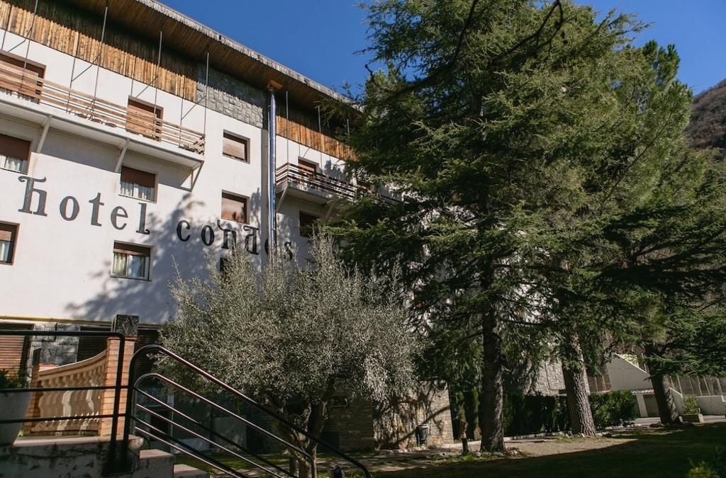 A hotel with a sign reading 'Hotel Conia.' It features a modern building with balconies and a staircase leading to the entrance.