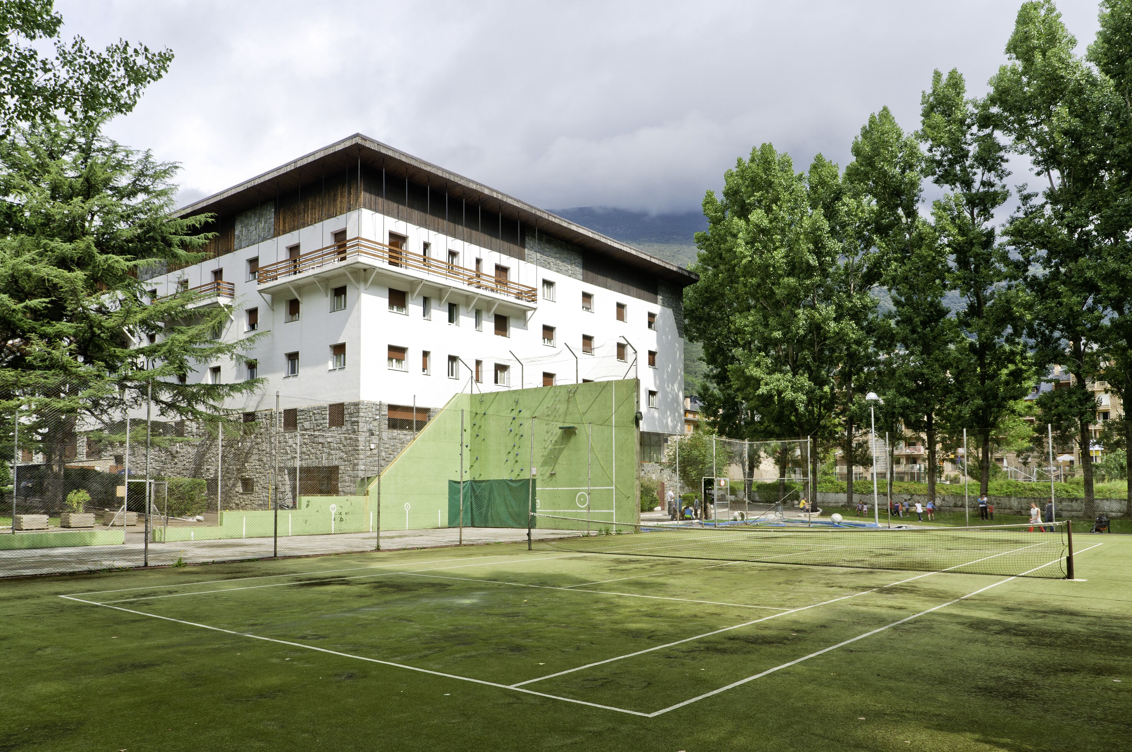 A tennis court adjacent to a building with multiple balconies and a stone facade.
