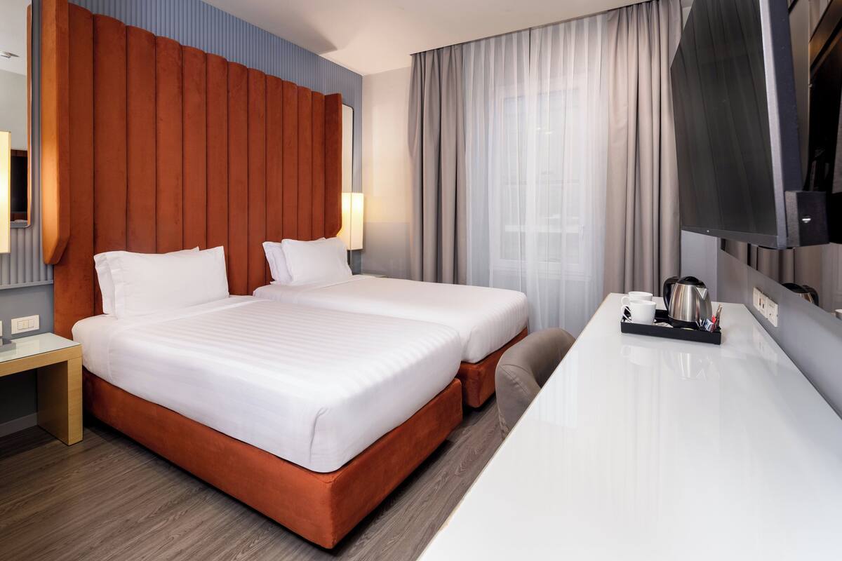 A hotel room with two beds, a desk, a TV, and a coffee tray.