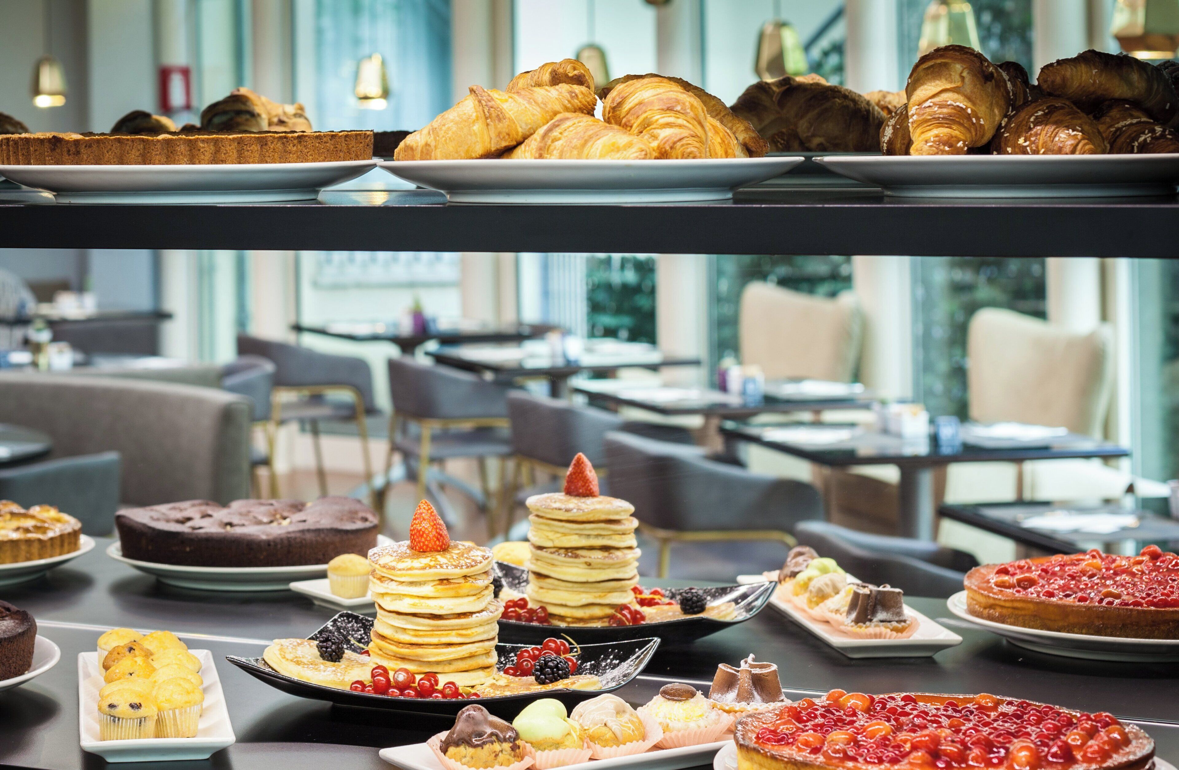 En buffet med et udvalg af desserter, herunder kager, wienerbrød og pandekager med frugt.