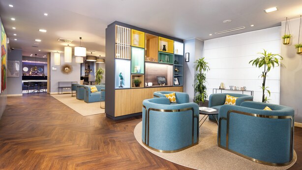 A modern hotel lobby with blue armchairs, a wooden reception desk, and a herringbone wood floor. - Holiday Inn Milan - Garibaldi Station by IHG (Milan)