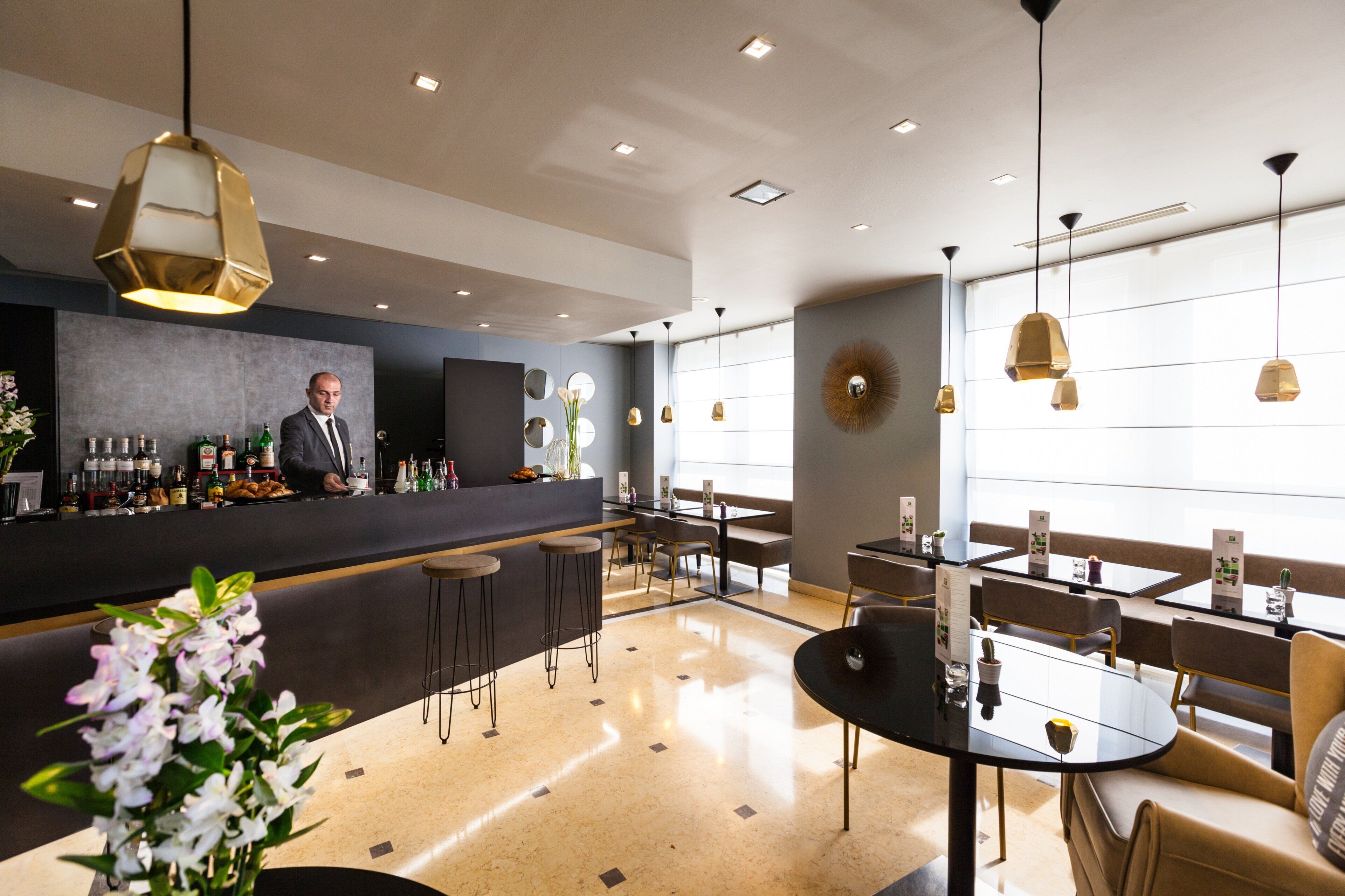 A modern bar area with a bartender, bar stools, and a counter displaying various bottles.